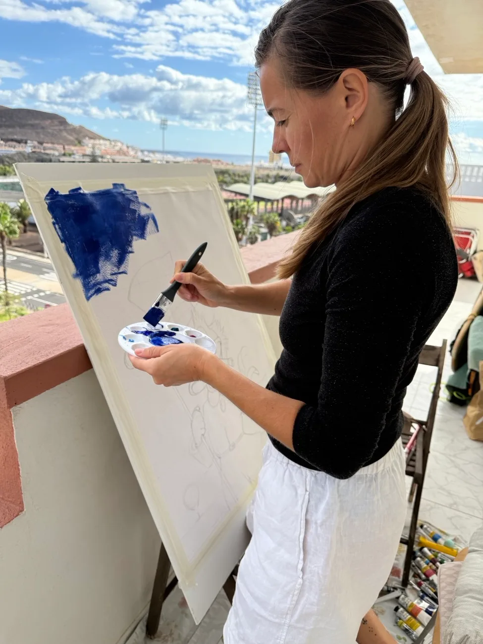 Maria pintando un lienzo en la terraza del estudio, con la costa de Tenerife detrás