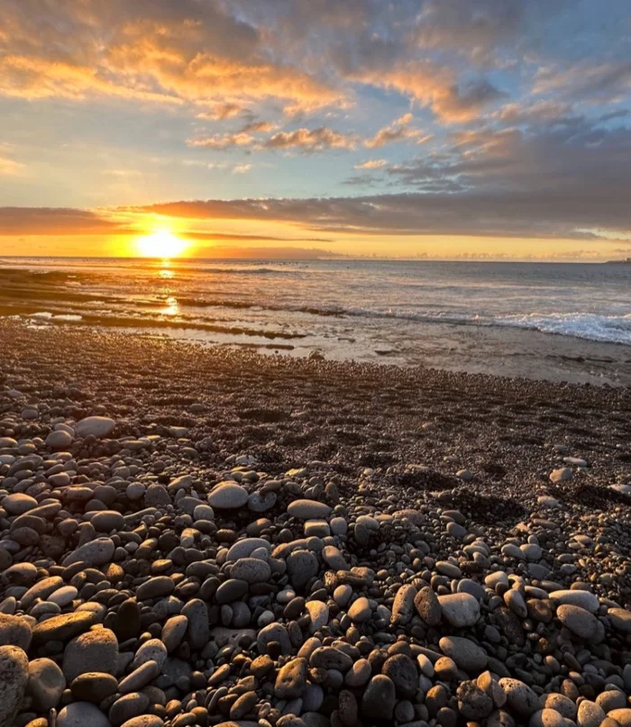 El sol bajo encendiendo los callaos de la playa en la golden hour