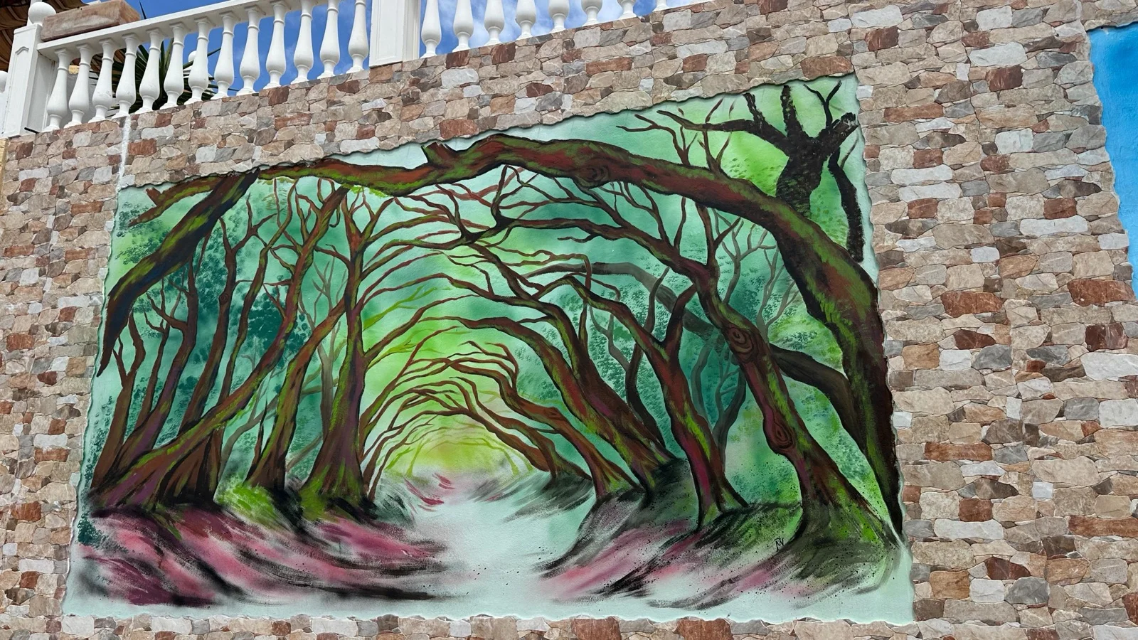 Mural de un bosque de laurisilva pintado por María en un muro de piedra, en la calle
