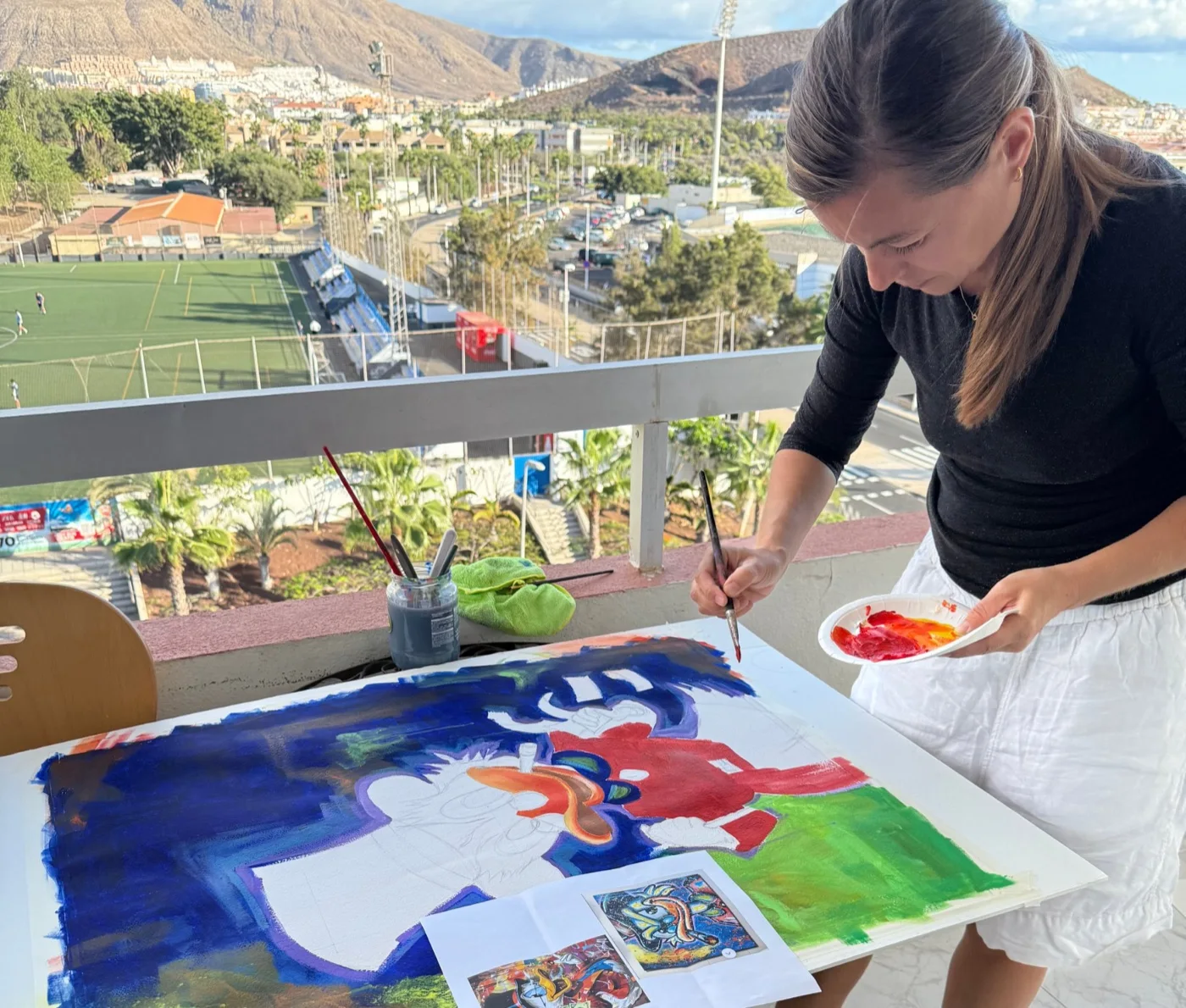 María pintando una obra de gran formato sobre la mesa de trabajo, con la paleta en la mano