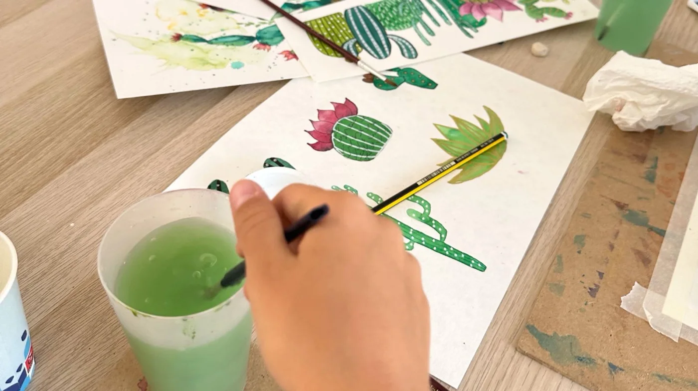 Manos pintando una acuarela de cactus en la mesa del estudio